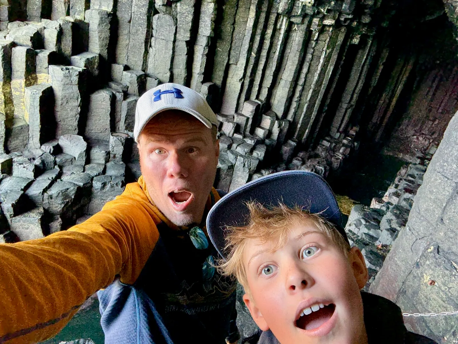 Selfie dvou lidí v jeskyni s čedičovými sloupy v pozadí, jeden z nich dává překvapený výraz.