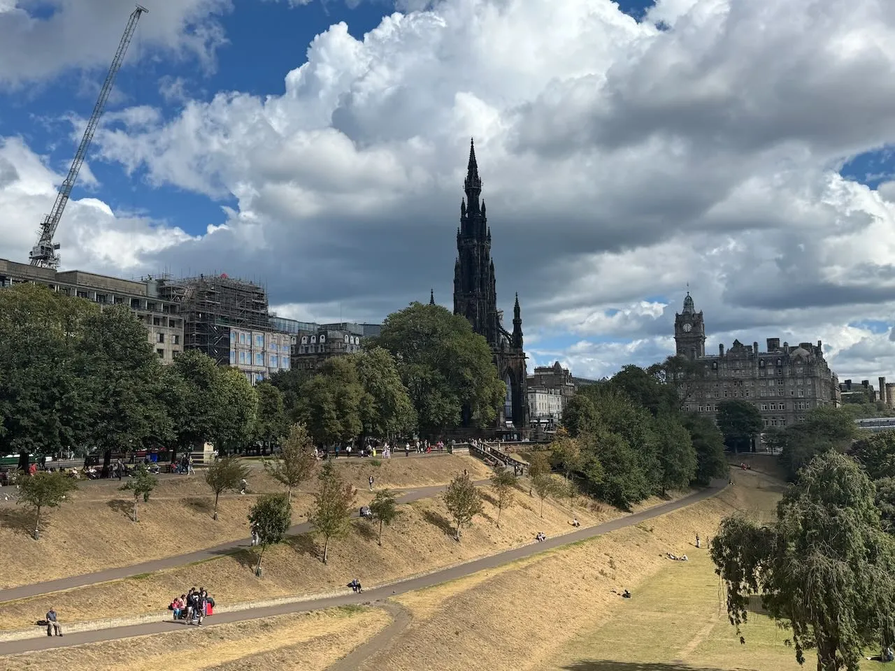 Pohled na Edinburgh s historickou architekturou, včetně Scott Monument, modré obloze a lehkými mraky.
